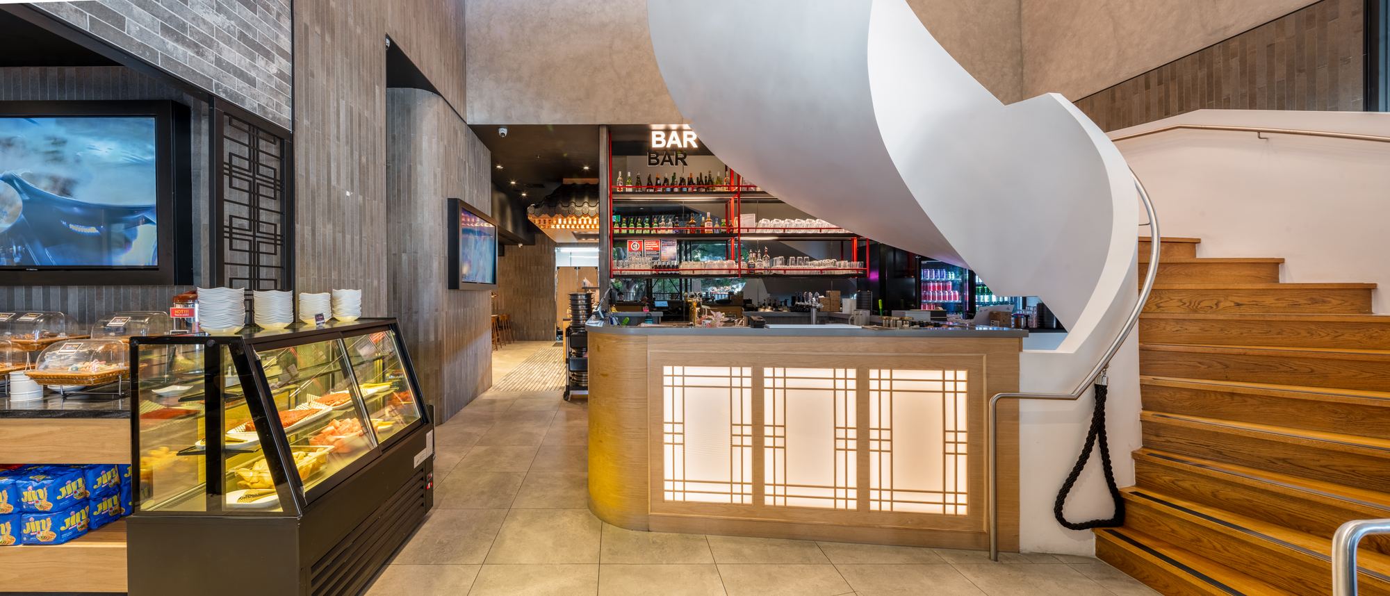 Bar with backlit timber lattice front beneath a curved white stair