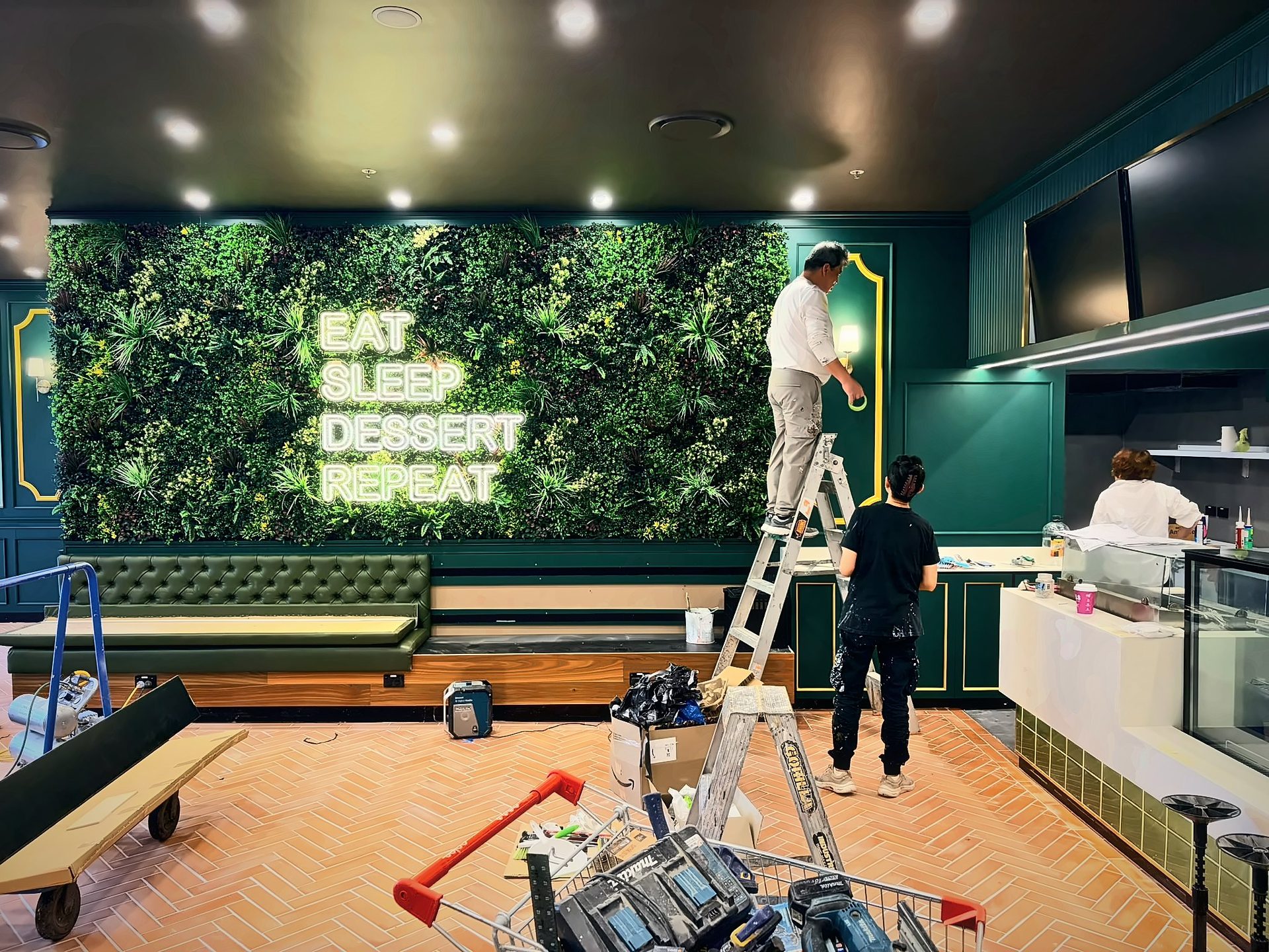 Green wall with EAT SLEEP DESSERT REPEAT neon, brass sconces and tufted banquette